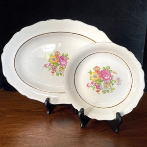 Puede incluir: Un juego de dos platos de servir de cerámica blanca con ribetes dorados y diseños florales. El plato más grande es de forma ovalada y el plato más pequeño es redondo.