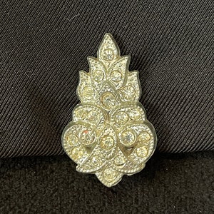 May include: A silver-toned brooch with a floral design, featuring a cluster of clear rhinestones.