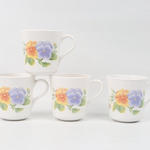 May include: Four white ceramic mugs with a floral design featuring yellow and purple pansies. The mugs have a white background and a simple handle.
