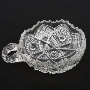 Puede incluir: Un cuenco de vidrio transparente con un diseño de vidrio cortado y un asa. El cuenco es perfecto para servir aperitivos o postres.