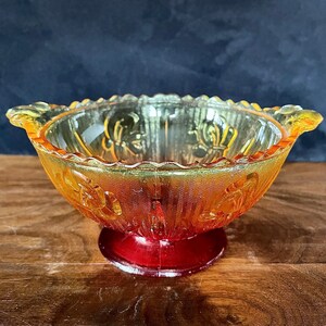 May include: A vintage glass bowl with a red base and yellow and orange glass design. The bowl has a scalloped rim and a decorative floral pattern.