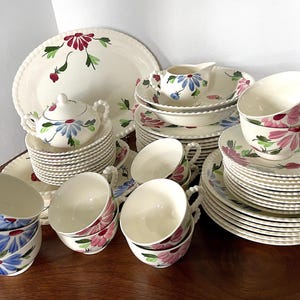 May include: A vintage floral china dinnerware set with a white background and blue, pink, and green floral designs. The set includes plates, bowls, cups, and saucers.