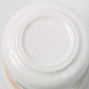 May include: White ceramic bowl with a floral design. The bottom of the bowl has the words "Corning Made in USA" printed on it.