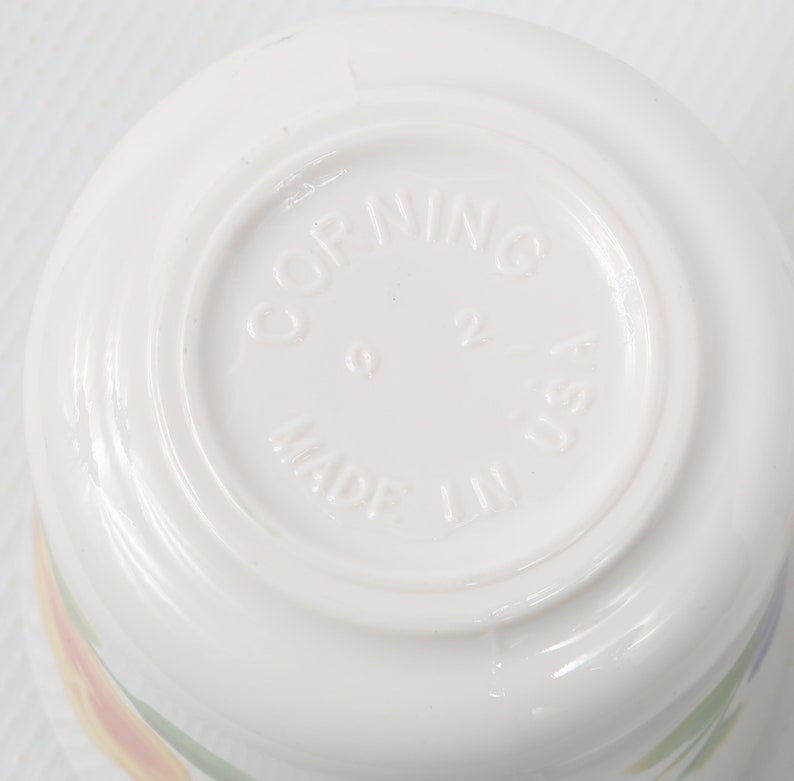 May include: White ceramic bowl with a floral design. The bottom of the bowl has the words "Corning Made in USA" printed on it.