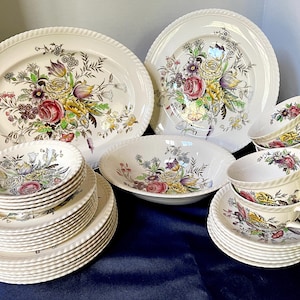 May include: A collection of vintage floral patterned china. The set includes serving platters, bowls, plates, saucers, and teacups. The floral design features red, yellow, purple, and green flowers. The edges of the plates and platters have a textured, rope-like design.