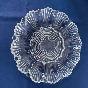 Peut inclure: Plat de service en verre transparent avec un bord festonné et un motif central en forme d'éclat d'étoile. Le plat est de forme circulaire avec des lignes rayonnantes, créant un aspect texturé. Idéal pour servir des amuse-gueules ou des collations.