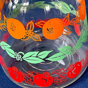 May include: Clear glass pitcher with a colorful fruit design. The pitcher features orange, red, and green fruit and leaf patterns. The design includes oranges, tomatoes, and leaves, creating a vibrant and decorative look. Ideal for serving beverages.