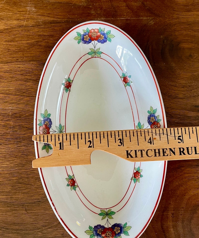 May include: White oval serving dish with a red and green floral design. The dish is 5 inches long.