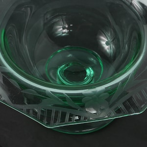 May include: A green glass bowl with an etched floral design. The bowl has a scalloped edge and a pedestal base.