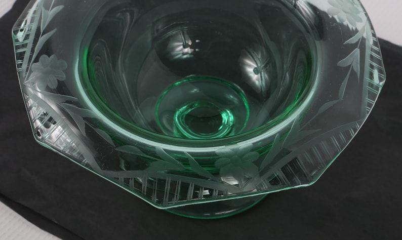 May include: A green glass bowl with an etched floral design. The bowl has a scalloped edge and a pedestal base.