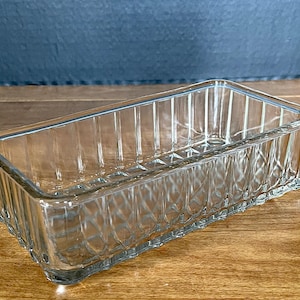 May include: A rectangular clear glass dish featuring vertical ribbed sides and a textured diamond pattern along the base. The container has an open top and a smooth, flat rim, providing a transparent and structured design for various storage needs.