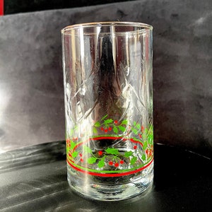 May include: A clear glass drinking glass with a textured surface and a red and green holly design around the top.