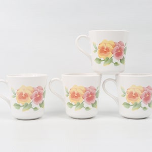 May include: Set of four white ceramic mugs with a floral design. Each mug features a yellow and pink pansy flower with green leaves.