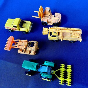 May include: A collection of toy construction vehicles, including a yellow pickup truck, a forklift, a bulldozer, a fire truck, and a tractor. The toys are in various shades of yellow, orange, and green, set against a blue background.