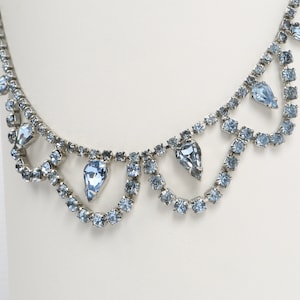 May include: A silver necklace with a teardrop-shaped design featuring light blue rhinestones.