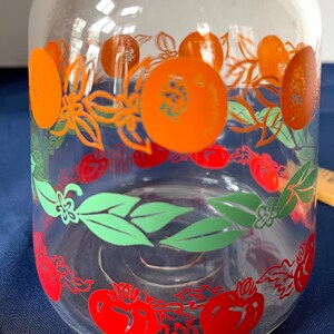 May include: Clear glass pitcher with a decorative fruit design. The pitcher features orange, red, and green illustrations of oranges, tomatoes, and leaves. The design wraps around the pitcher, creating a vibrant and colorful aesthetic.