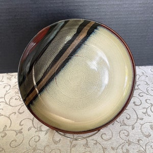 May include: A large, round ceramic bowl with a cream-coloured interior and a dark brown, black, and gold striped exterior.