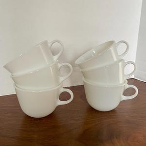 Könnte beinhalten: Sechs weiße Keramikbecher mit Henkeln, die ineinander gestapelt sind. Der obere Becher hat einen Henkel auf der rechten Seite und der untere Becher einen Henkel auf der linken Seite.