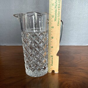 Op de afbeelding: Een heldere glazen kan met een diamantpatroon en een gegolfde rand. De kan is 18 cm hoog.