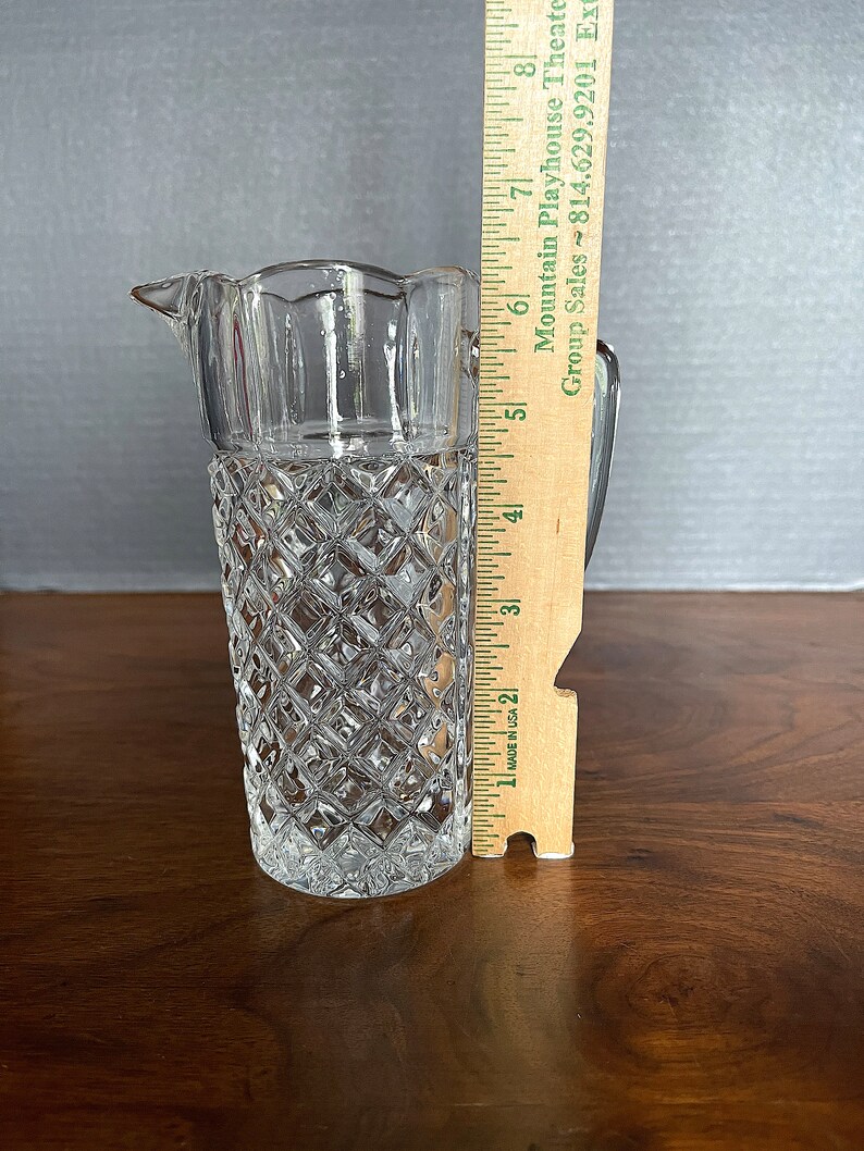 Op de afbeelding: Een heldere glazen kan met een diamantpatroon en een gegolfde rand. De kan is 18 cm hoog.
