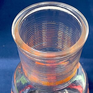 May include: Clear glass pitcher with a wide, ribbed neck and a colorful design on the lower portion. The pitcher has a slightly flared rim and a cylindrical neck. The design on the pitcher includes orange and green elements.