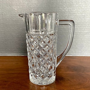 Op de afbeelding: Een glazen kan met een diamantpatroon. De kan heeft een handvat en een tuit.