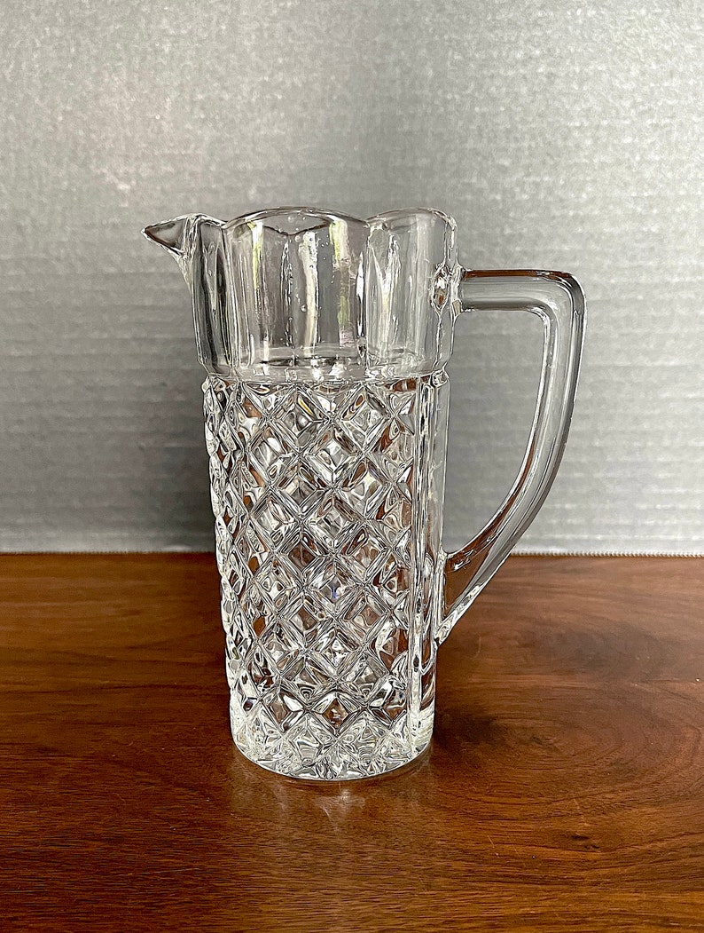 Op de afbeelding: Een glazen kan met een diamantpatroon. De kan heeft een handvat en een tuit.