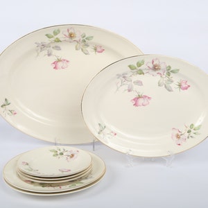 May include: A set of five white oval plates with a gold rim and a floral design featuring pink roses and green leaves.