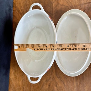 May include: White oval ceramic serving dish with a floral pattern and a matching lid. The dish is 7 inches long.