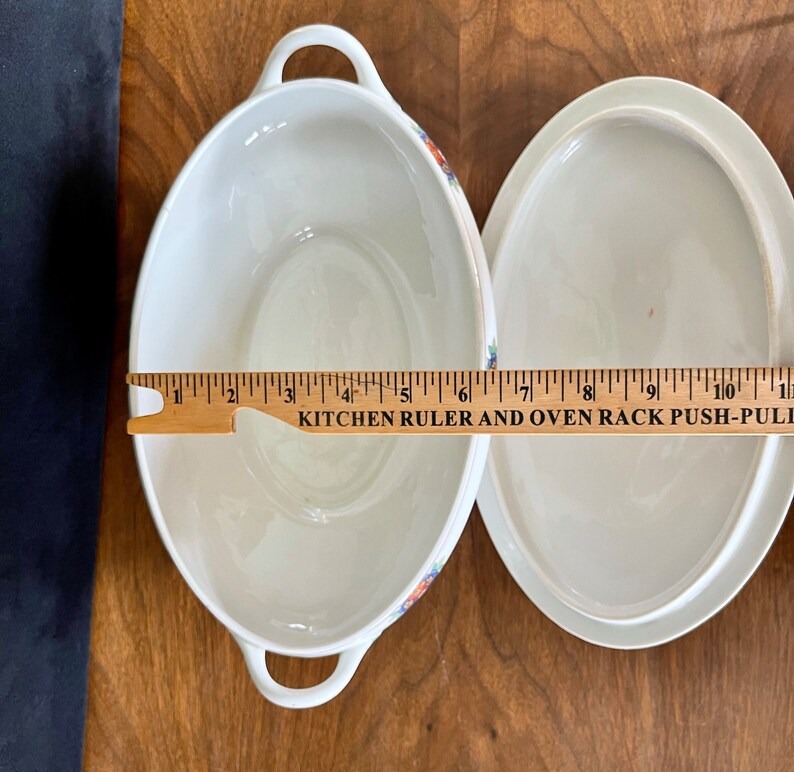 May include: White oval ceramic serving dish with a floral pattern and a matching lid. The dish is 7 inches long.