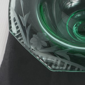 May include: A green glass bowl with an etched floral design. The bowl has a scalloped edge and is made of clear glass.