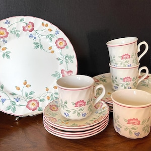 Könnte beinhalten: Ein Set aus floral gemusterten Porzellan-Teetassen und Untertassen. Die Tassen und Untertassen haben ein zartes Blumenmuster mit rosa, roten und grünen Akzenten. Das Set enthält einen großen Speiseteller mit einem passenden Blumenmuster.