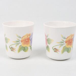 May include: Two white ceramic mugs with a floral design featuring yellow, pink, and purple pansies. The mugs have a simple, elegant design.
