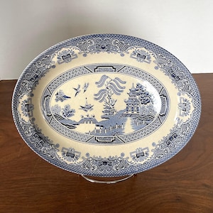 May include: A blue and white oval serving platter with a traditional Chinese design. The platter features a pagoda, willow branches, and a blue and white border.