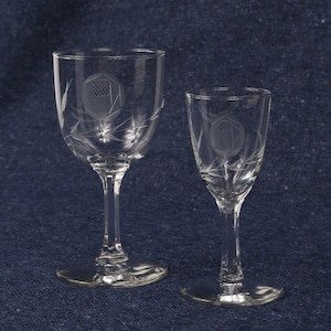 May include: Two clear glass drinking glasses with etched designs. The larger glass has a wider bowl and a taller stem. The smaller glass has a narrower bowl and a shorter stem.