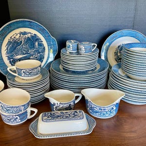 Puede incluir: Un juego de vajilla vintage de porcelana azul y blanca con un diseño escénico. El juego incluye platos, cuencos, tazas, platillos y una mantequillera.