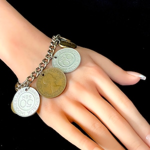 Puede incluir: Un brazalete de cadena de plata con varias monedas de plata y oro unidas. Las monedas presentan varios diseños y textos, incluyendo "REPUBLIK INDONESIA" y "50 SEN".