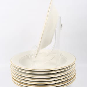 May include: A stack of eight white ceramic soup bowls with a gold rim. The bowls are stacked on a white surface.