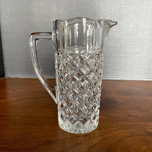 Op de afbeelding: Een glazen kan met een diamantpatroon. De kan heeft een handvat en een tuit.