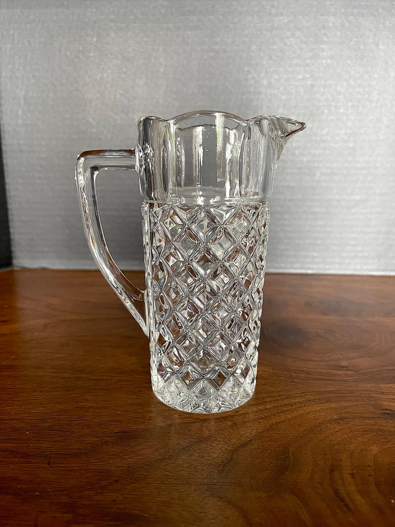 Op de afbeelding: Een glazen kan met een diamantpatroon. De kan heeft een handvat en een tuit.