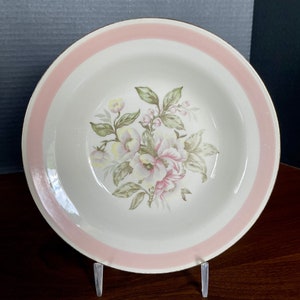 May include: A white ceramic bowl with a pink and gold rim. The bowl features a floral design with pink and yellow flowers and green leaves.
