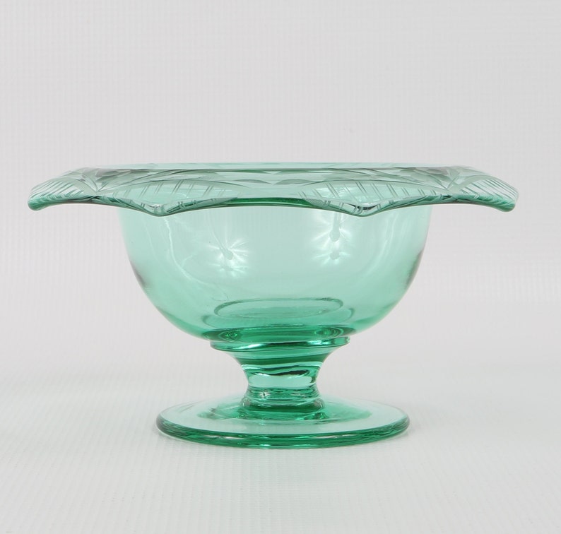 May include: A green glass pedestal bowl with a scalloped rim and a decorative etched design.