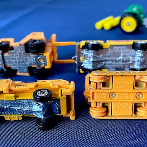 May include: A collection of toy construction vehicles, including a yellow dump truck, a bulldozer, and a green tractor. The toys are made of metal and plastic, with black wheels. The vehicles are arranged on a blue surface.