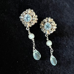 May include: A pair of silver dangle earrings with blue gemstones and white pearls. The earrings feature a floral design.