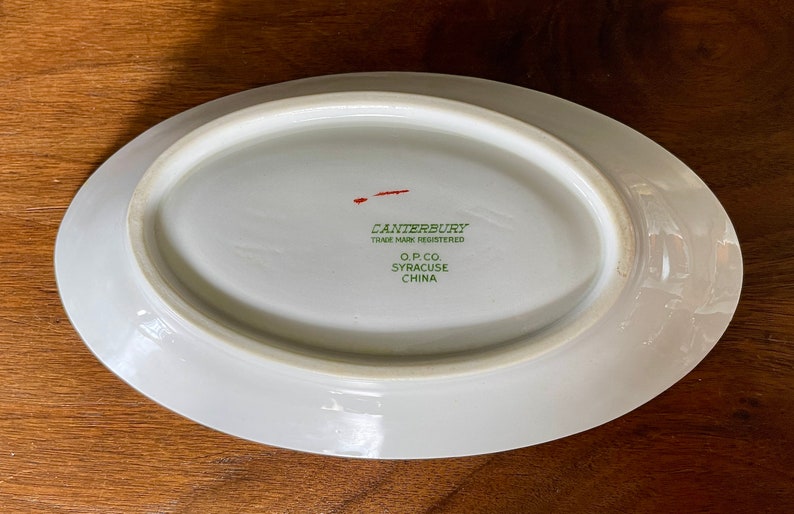 May include: White oval ceramic dish with a green and red inscription that reads "Canterbury Trade Mark Registered O.P. Co. Syracuse China".
