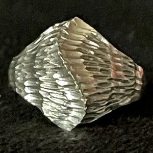 May include: A silver ring with a textured, diamond-shaped design. The ring is made of metal and has a rough, hammered finish.
