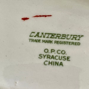 May include: Close-up of a white ceramic plate with green text that reads "Canterbury Trade Mark Registered O.P.Co. Syracuse China".