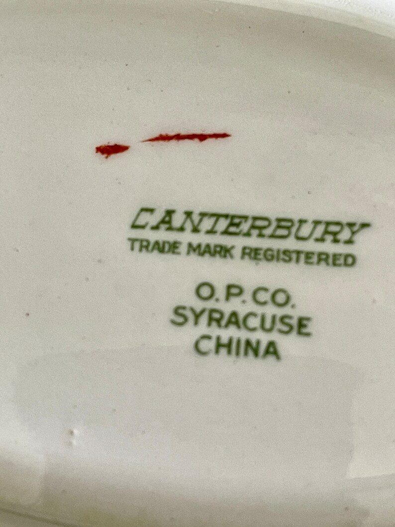 May include: Close-up of a white ceramic plate with green text that reads "Canterbury Trade Mark Registered O.P.Co. Syracuse China".