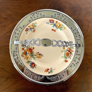 May include: A vintage, cream-colored serving dish with a floral pattern and a silver-plated handle. The dish has a decorative, openwork rim.
