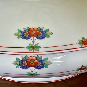 May include: White ceramic serving dish with a red and orange floral design. The dish has a scalloped edge and a red rim.